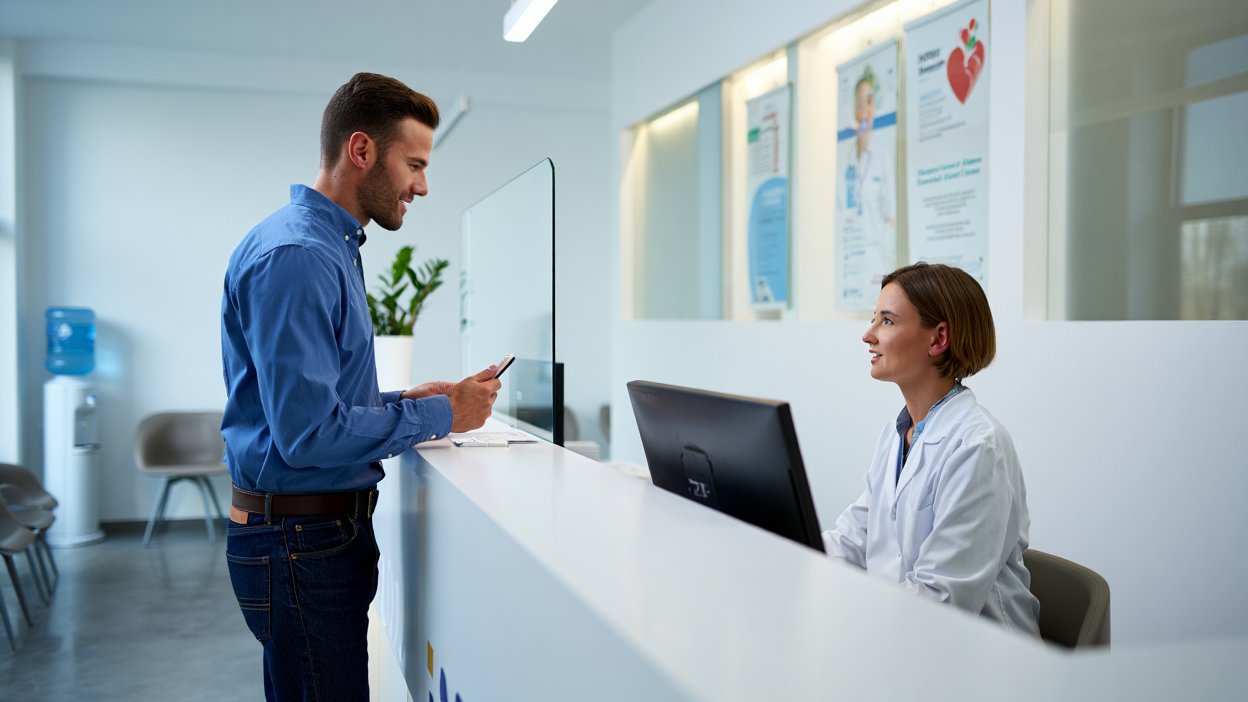 Мужчина стоит около стойки регистрации в больнице